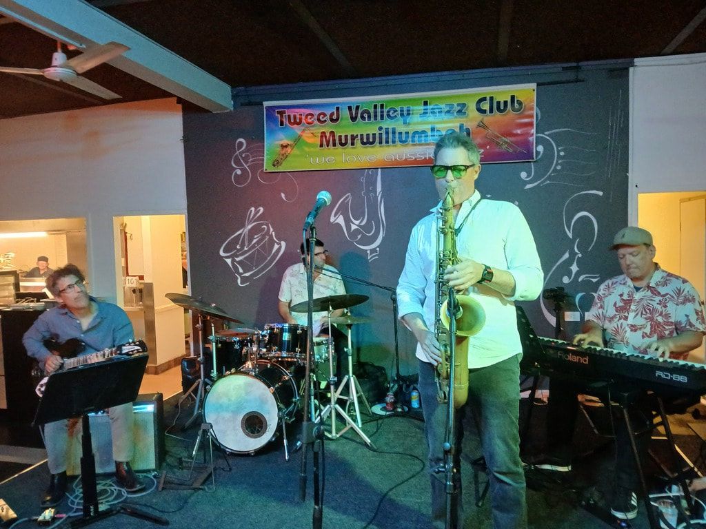 The Root Note on stage, with a saxophonist in front of the club's rainbow banner
