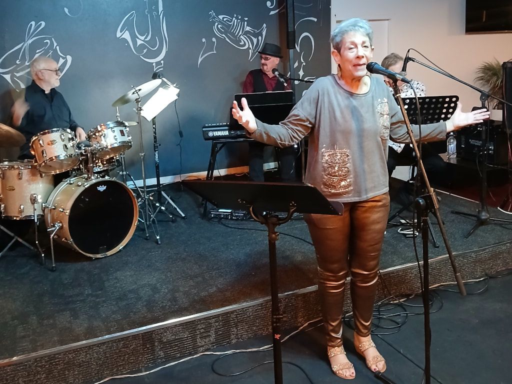 Vicki Salisbury singing with arms outstretched, with drums and keyboards behind her