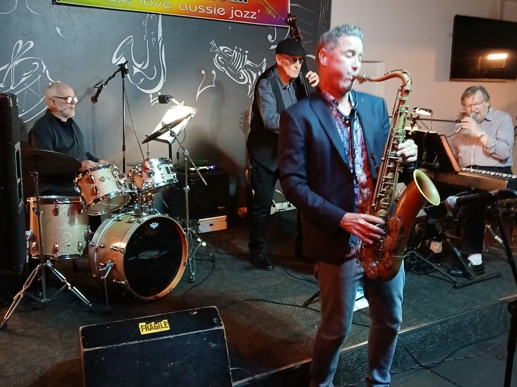 Adam Thomas playing tenor sax, with drums and keyboards behind him